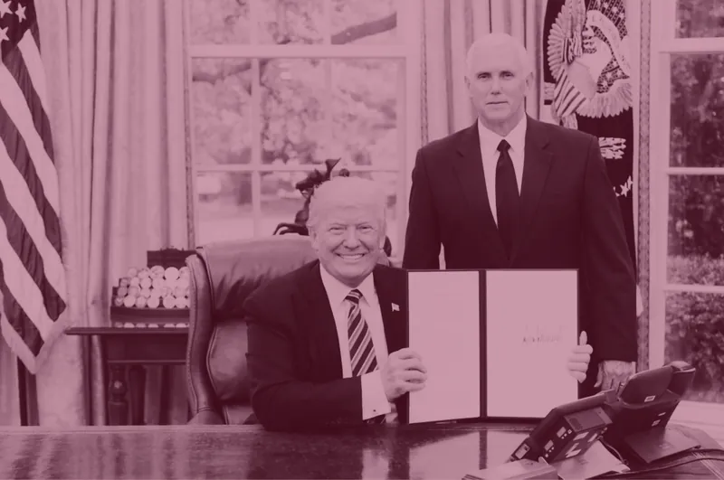 Red-tinted photo of President Trump holding up a signed document at a signing ceremony.